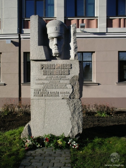 Oļega Skaraiņa granītā kalto pieminekli. Pieminekli veido trīs masīvu akmens bluķu obelisks ar pulkveža portretu augšdaļā un veltījuma tekstu vidū: 